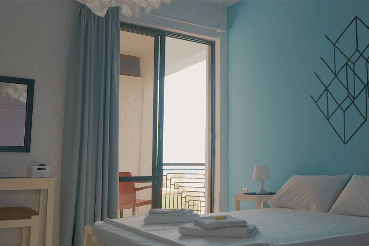Habitación de hotel con cama, escritorio, silla, ventana con cortinas y un adorno geométrico en la pared.