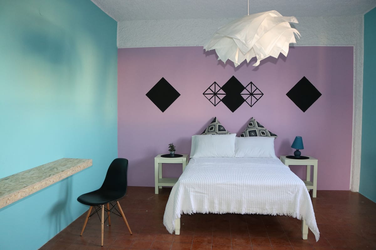 Un dormitorio con una cama, una silla, una mesita de noche y decoración en la pared.