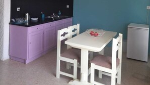 Une cuisine de taille réduite avec des meubles de couleur violette, une table blanche avec deux chaises, une horloge au mur et un petit réfrigérateur.