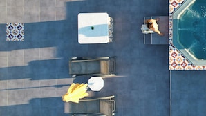 Vue aérienne d’un espace piscine aménagé sur un toit, avec des chaises longues, des parasols et une piscine.