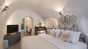 A bedroom with a curved ceiling, a bed with white bedding, a TV on a stand, and a decorative wall lamp. - Dandy Cave Villa-Private Luxurious Waterfall Pool - Hot Tub (Santorini)
