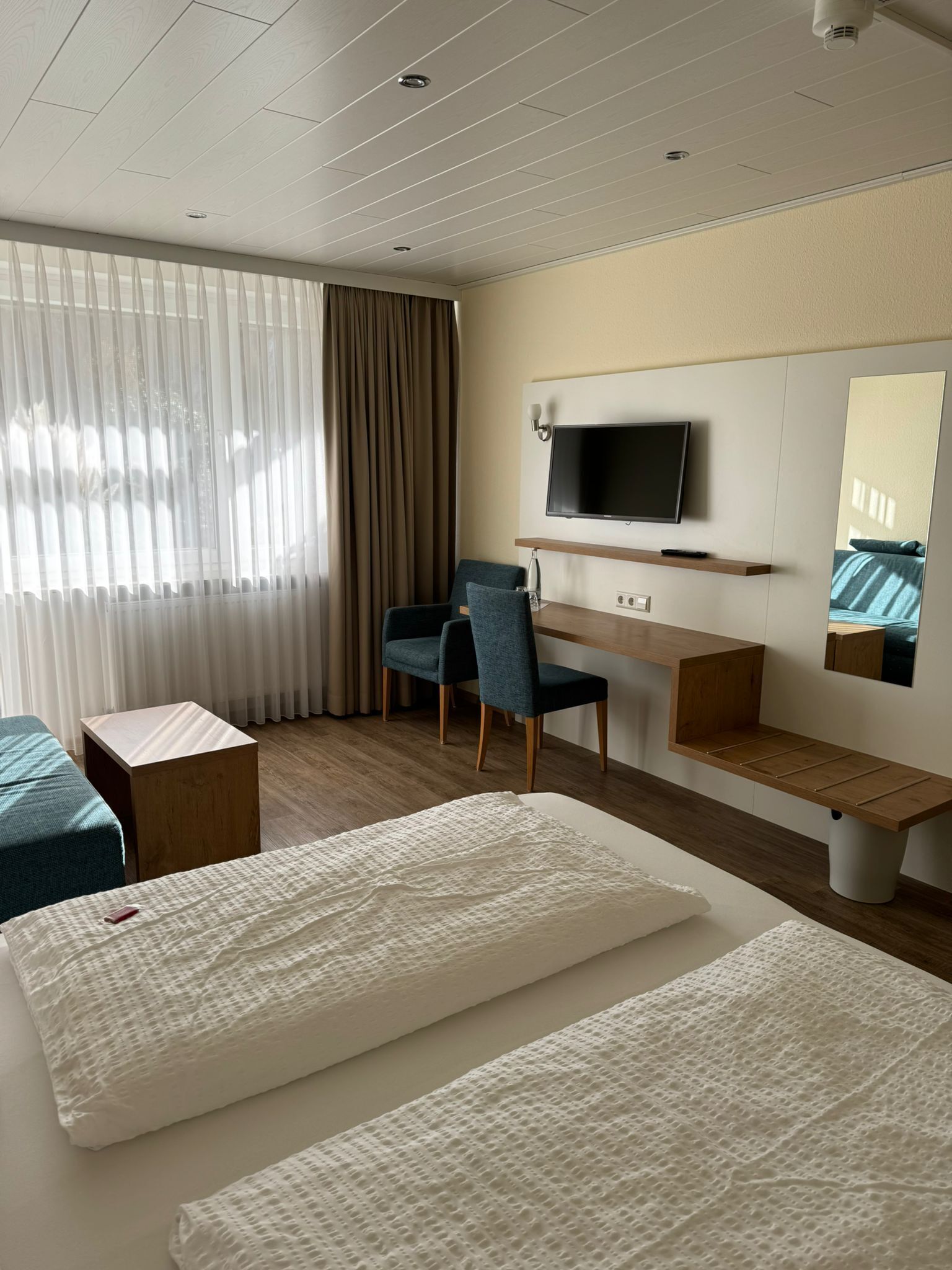 Een hotelkamer met twee bedden, een bureau, een stoel, een televisie en een groot raam met gordijnen.