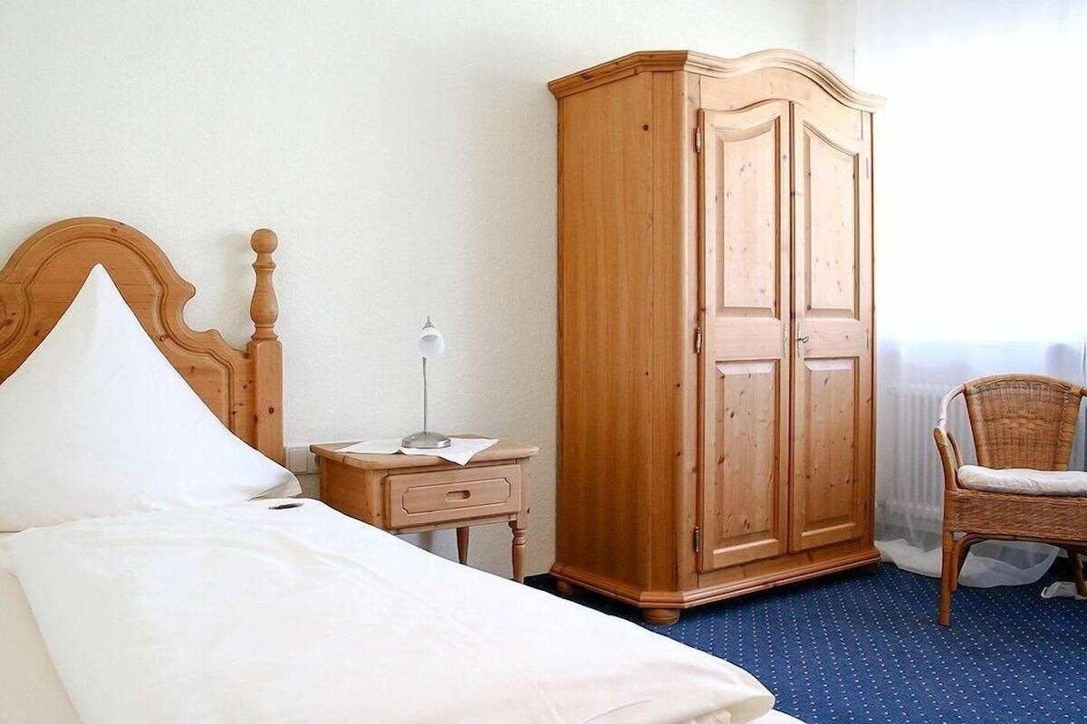 Une chambre à coucher avec un lit, une armoire en bois, une table de chevet avec une lampe et un fauteuil en osier.
