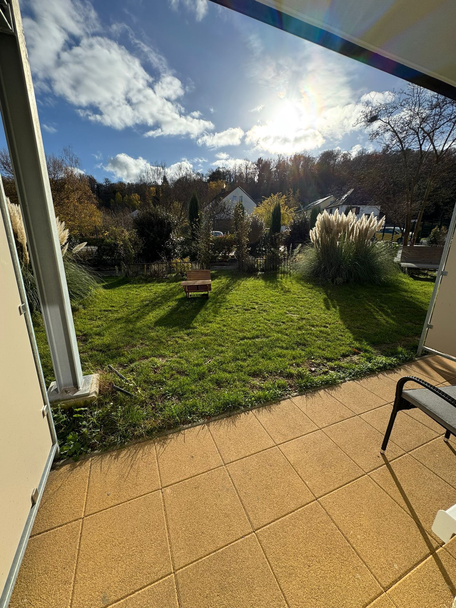 Un patio con vista a un jardín césped, un banco de madera y una casa al fondo.