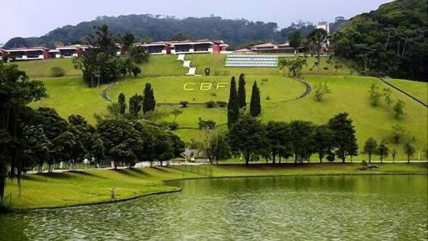 A golf course with a pond, surrounded by trees and buildings with the letters "CBF" visible. - Pousada Bariloche (Teresópolis)