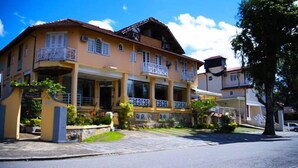 A two-story house with a balcony, a stone entrance, and a paved driveway. - Pousada Bariloche (Teresópolis)