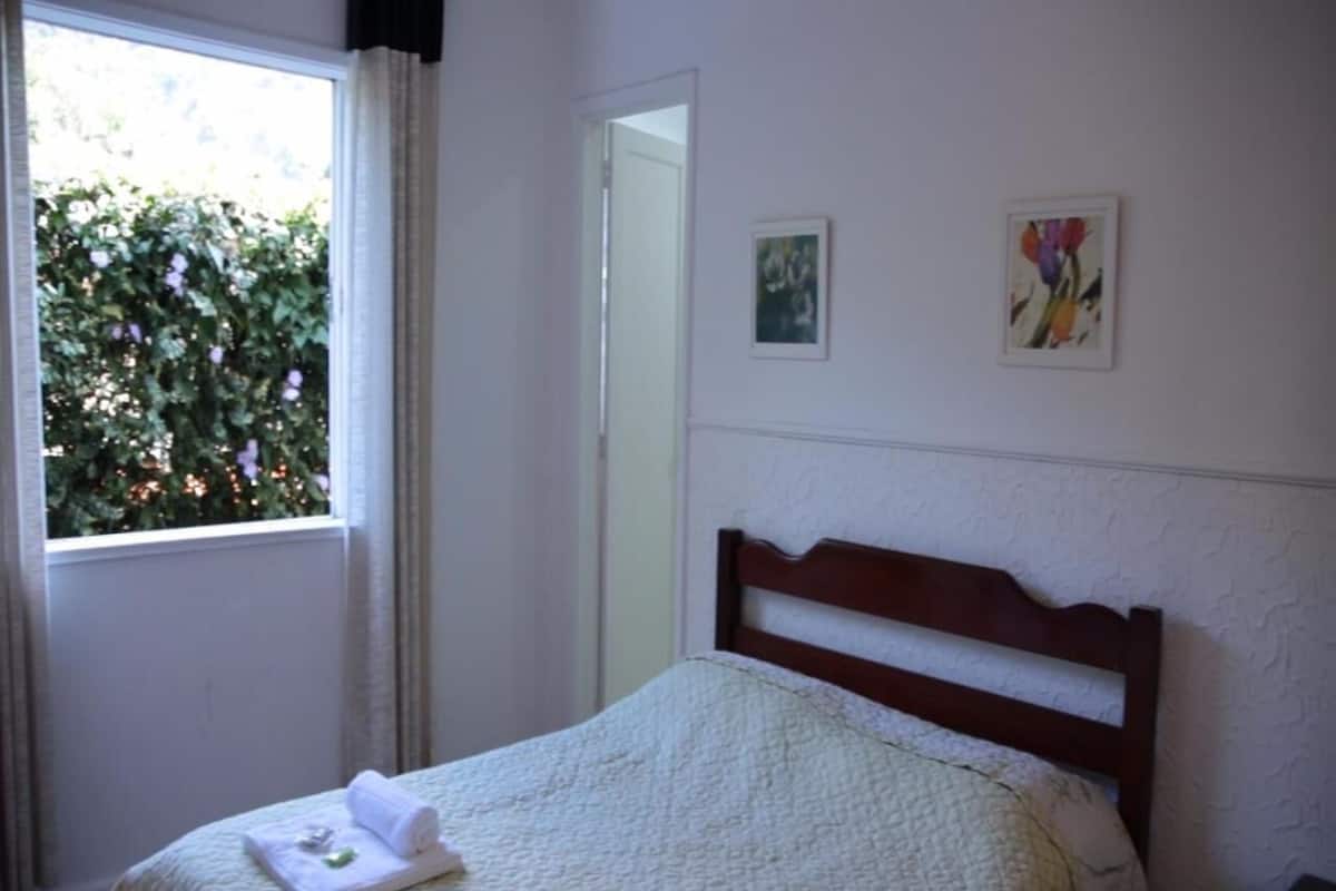 A neatly made bed with a white quilt and two towels, a window with curtains, and two framed artworks on the wall.