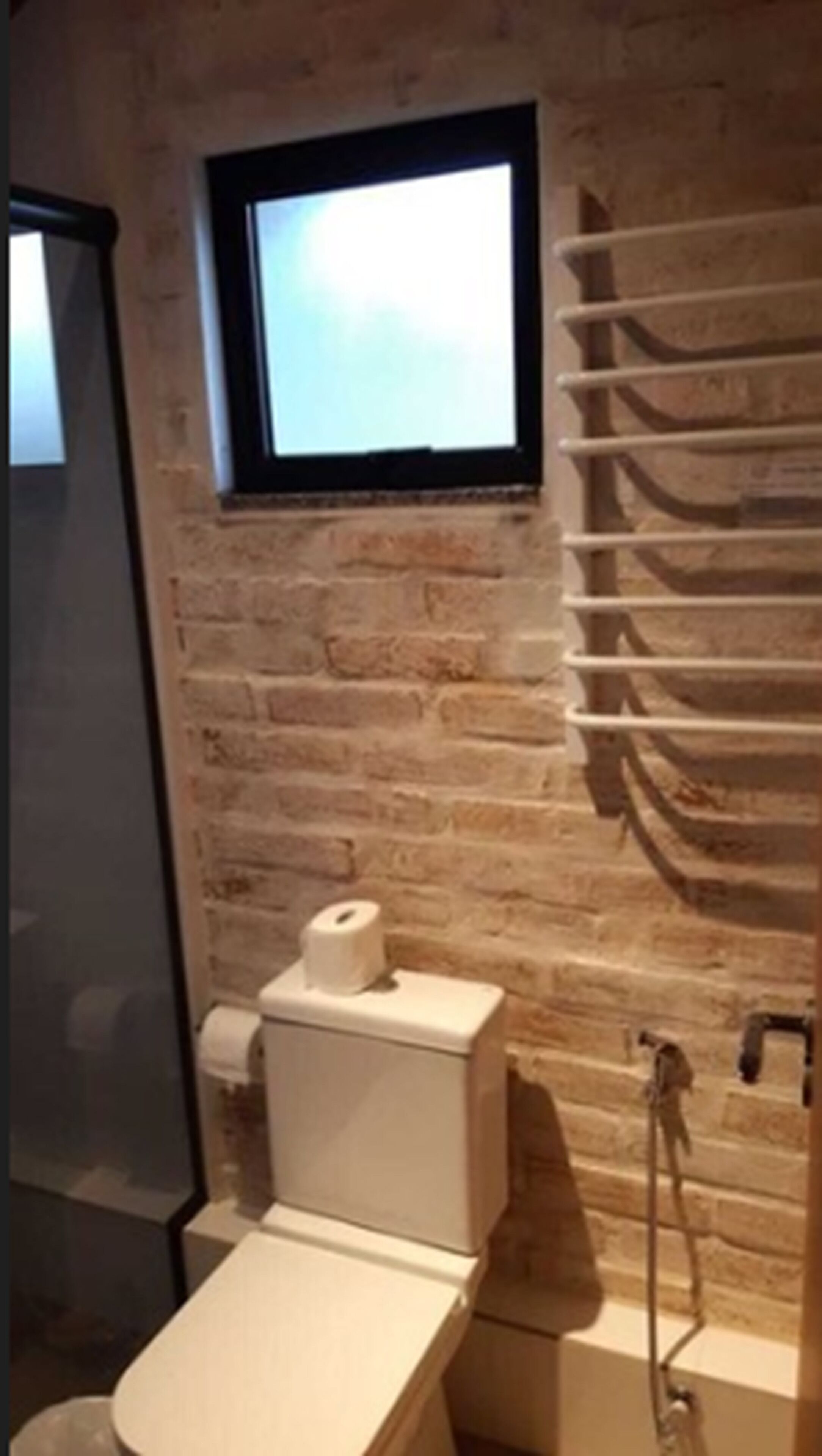 A bathroom with a brick wall, a toilet, a sink, and a window.