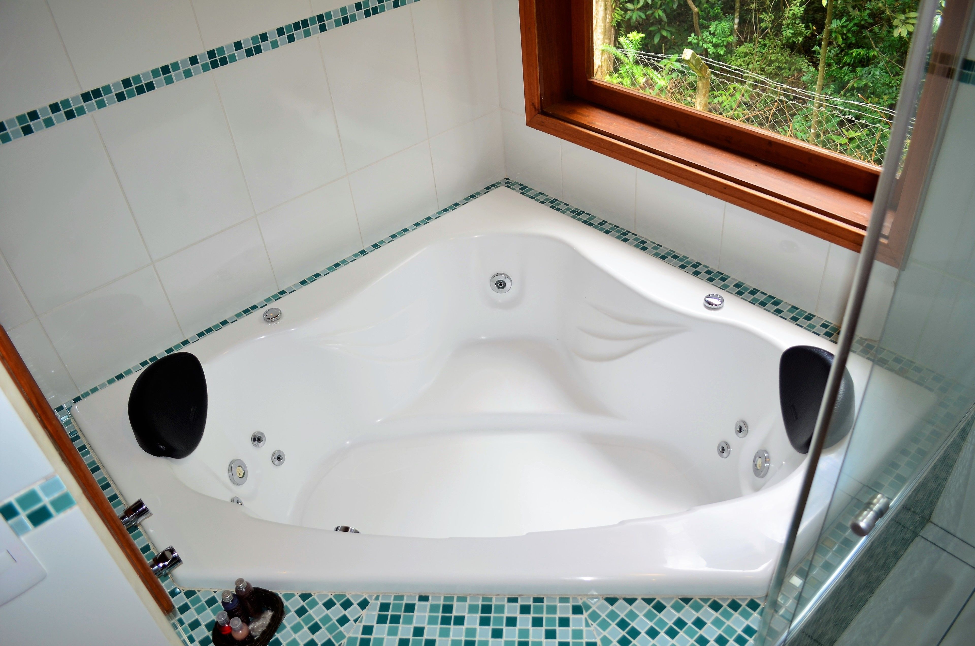 A large, freestanding bathtub with a window above it, surrounded by tiled walls.