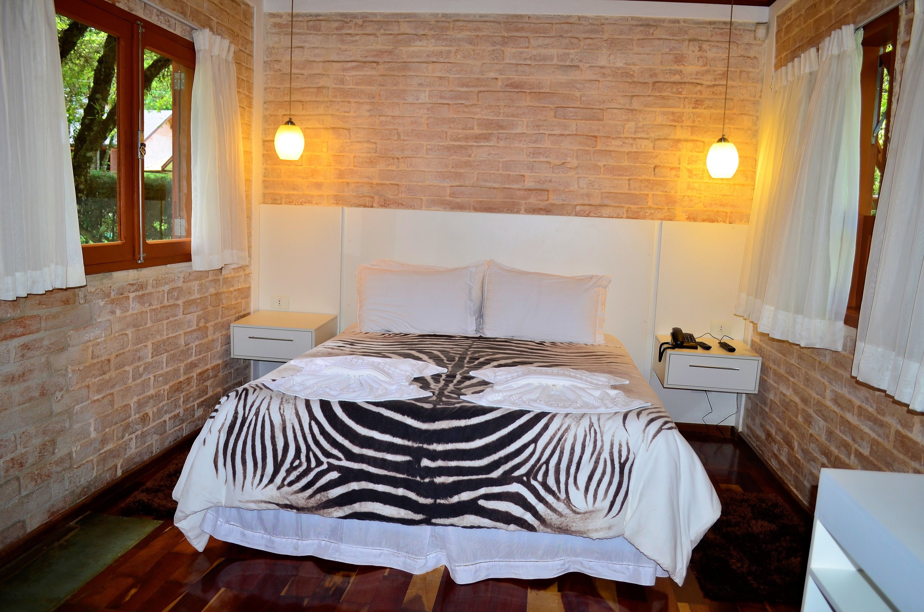 A bedroom with a zebra-patterned bedspread, brick walls, and two bedside lamps.