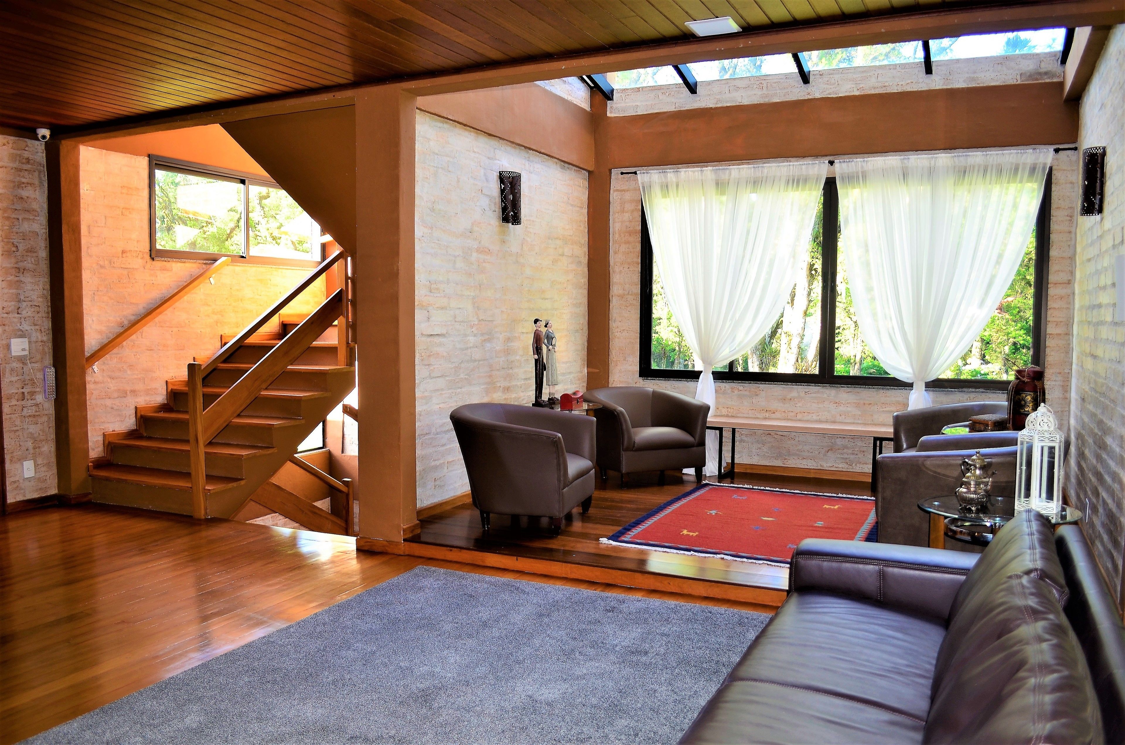 A spacious living area with a wooden staircase, leather sofas, and a red rug.