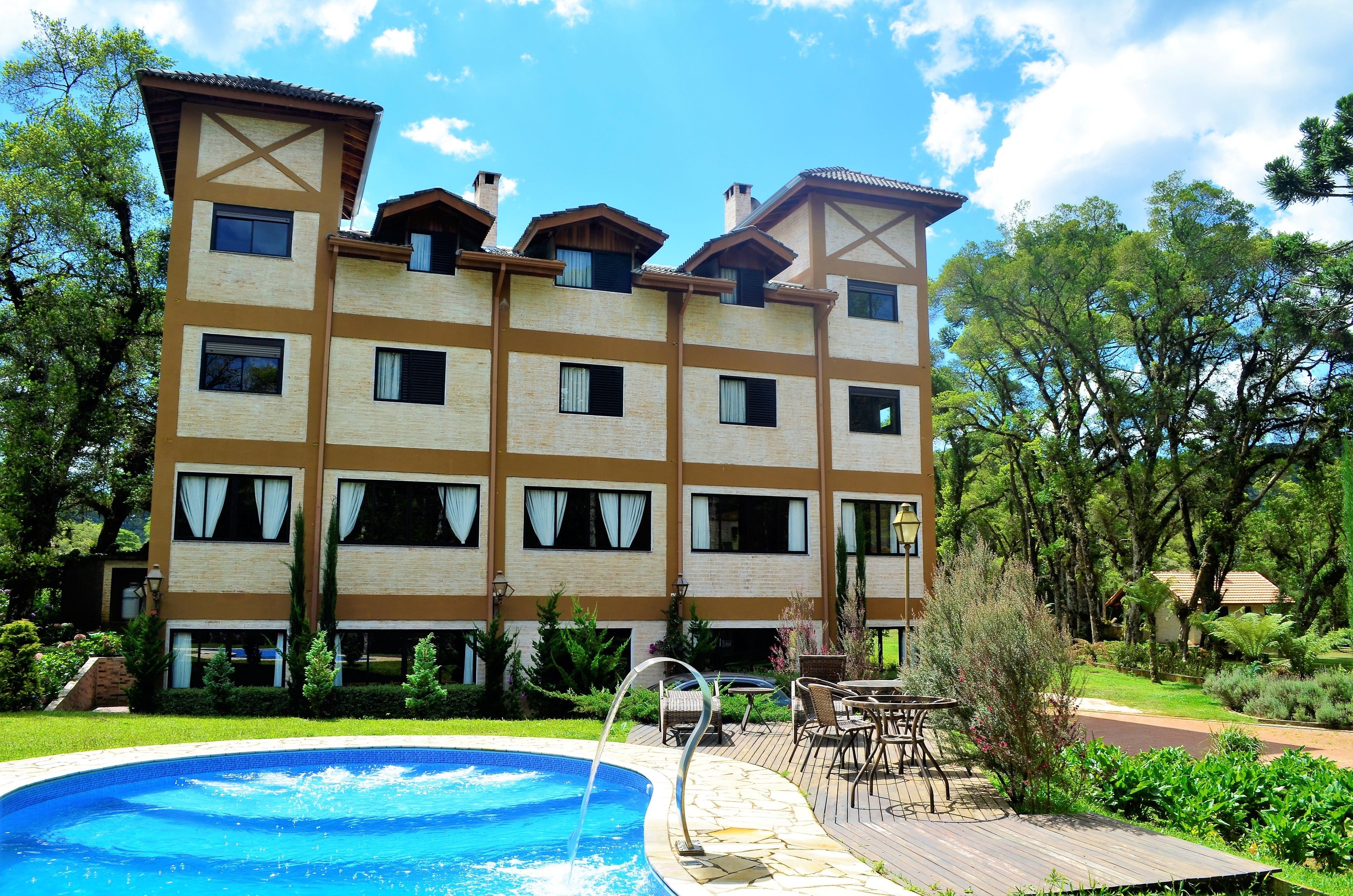 A multi-story hotel with a swimming pool, outdoor seating, and a garden.