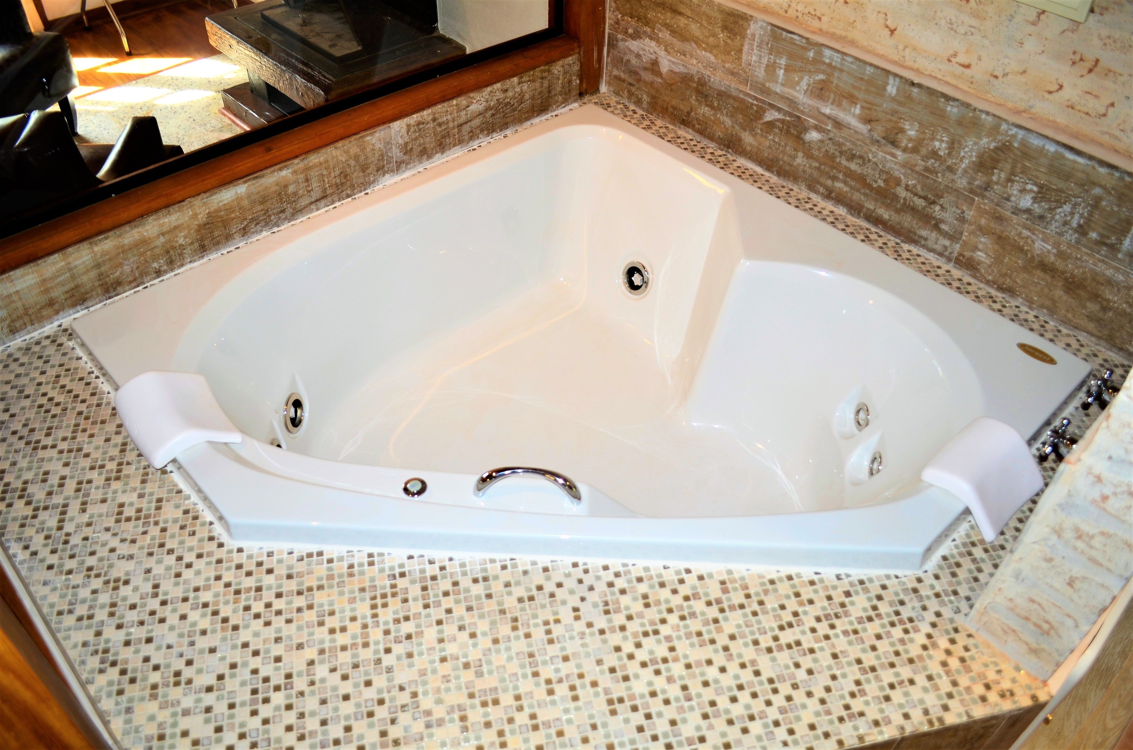 A large, rectangular bathtub with a chrome faucet and drain, set on a tiled floor with a mosaic pattern.