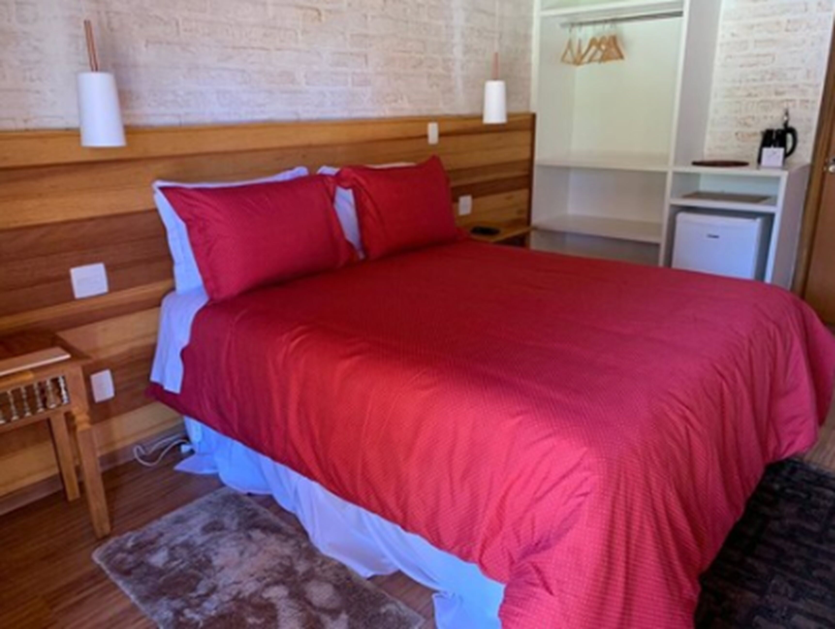 Una cama bien hecha con ropa de cama roja, un cabecero de madera y una mesita de noche pequeña con una lámpara.