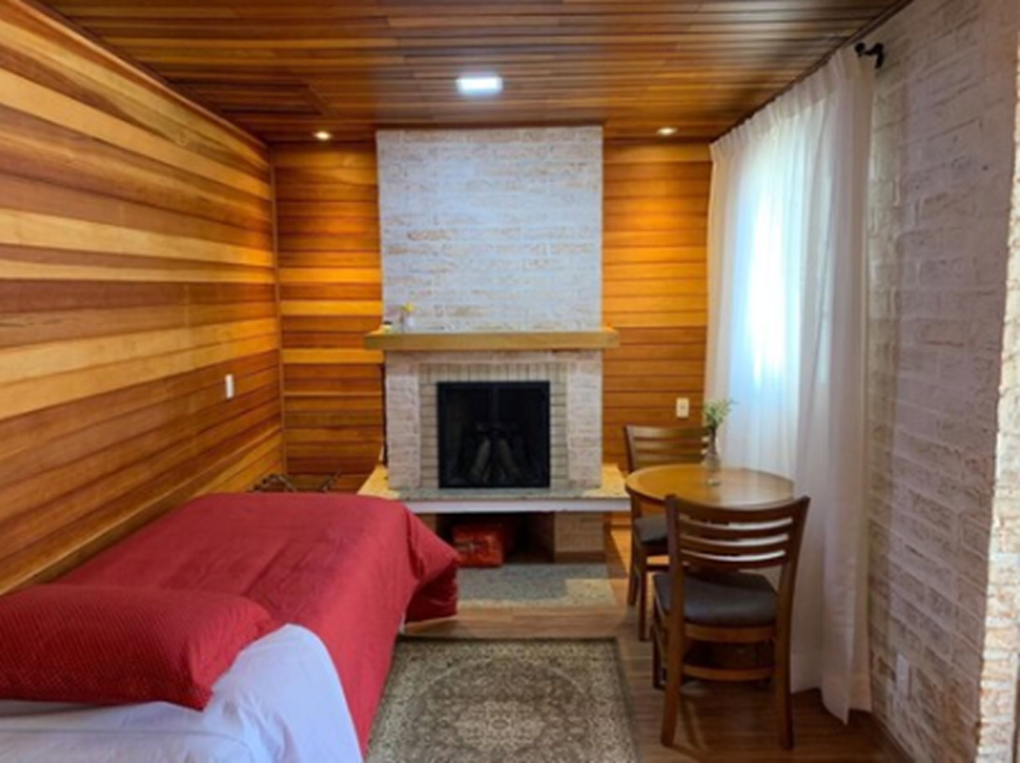 A cozy room with wooden walls, a fireplace, a bed, and a dining table with chairs.