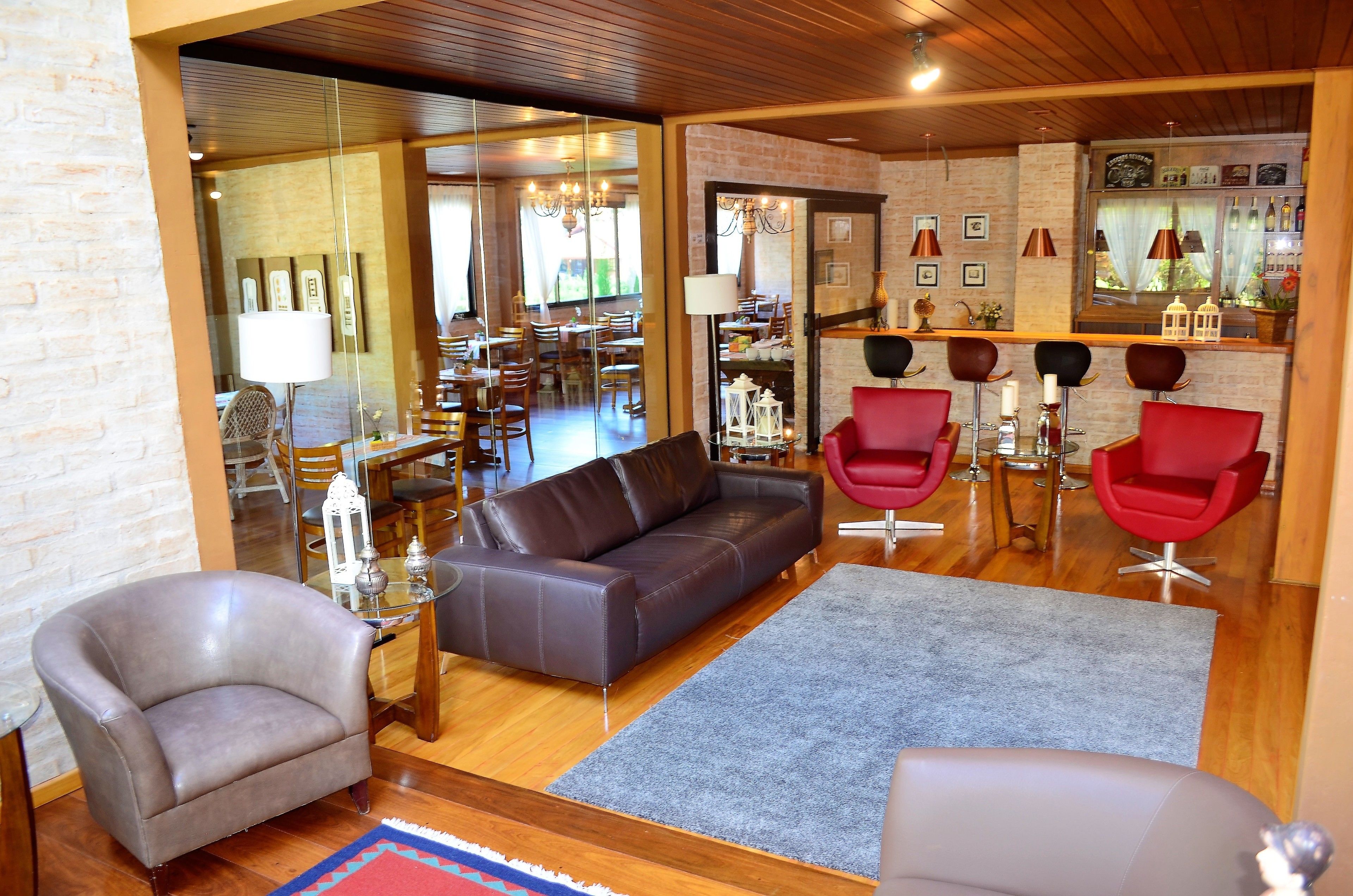 A modern living area with a leather sofa, two armchairs, and a dining table. A bar area with stools and a wine rack is visible in the background.