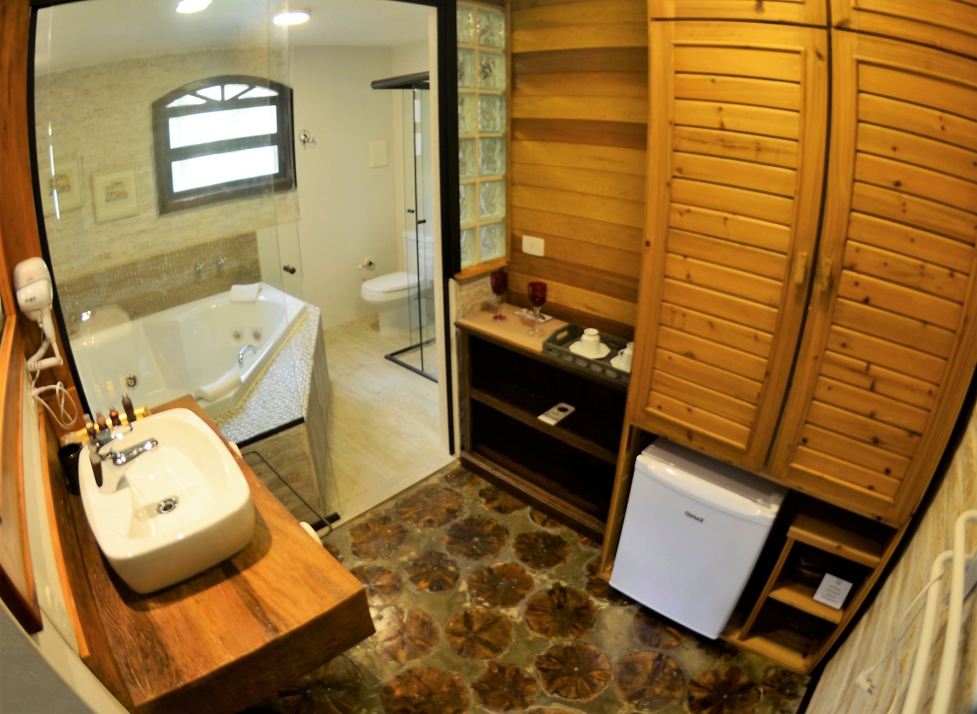 A bathroom with a bathtub, a sink, a small refrigerator, and wooden paneling.
