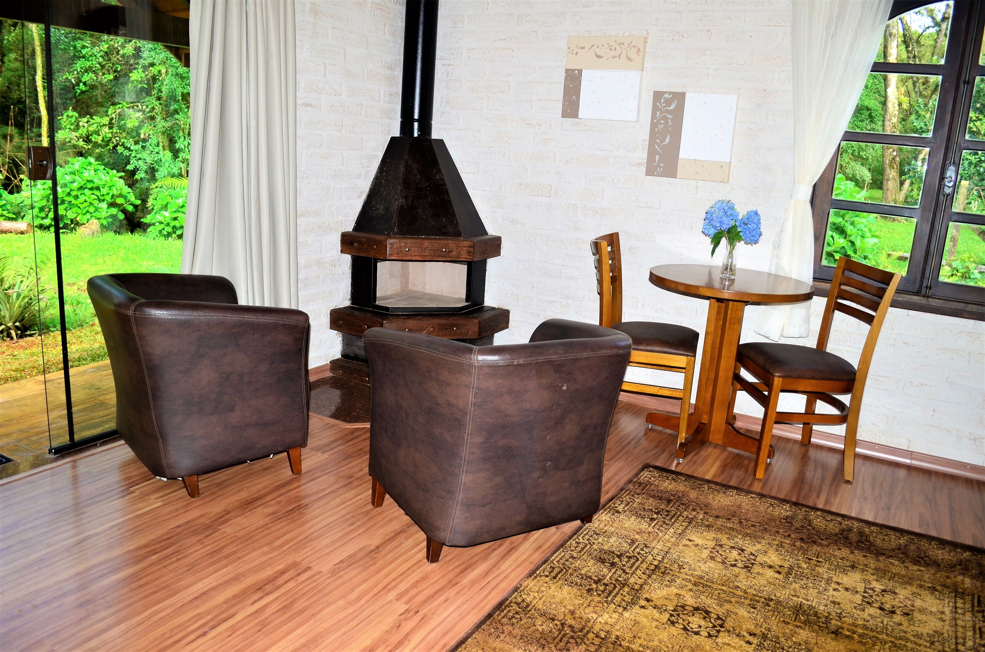 Un cuarto acogedor con chimenea, sillones de cuero, una mesa de madera y vistas al verdor.