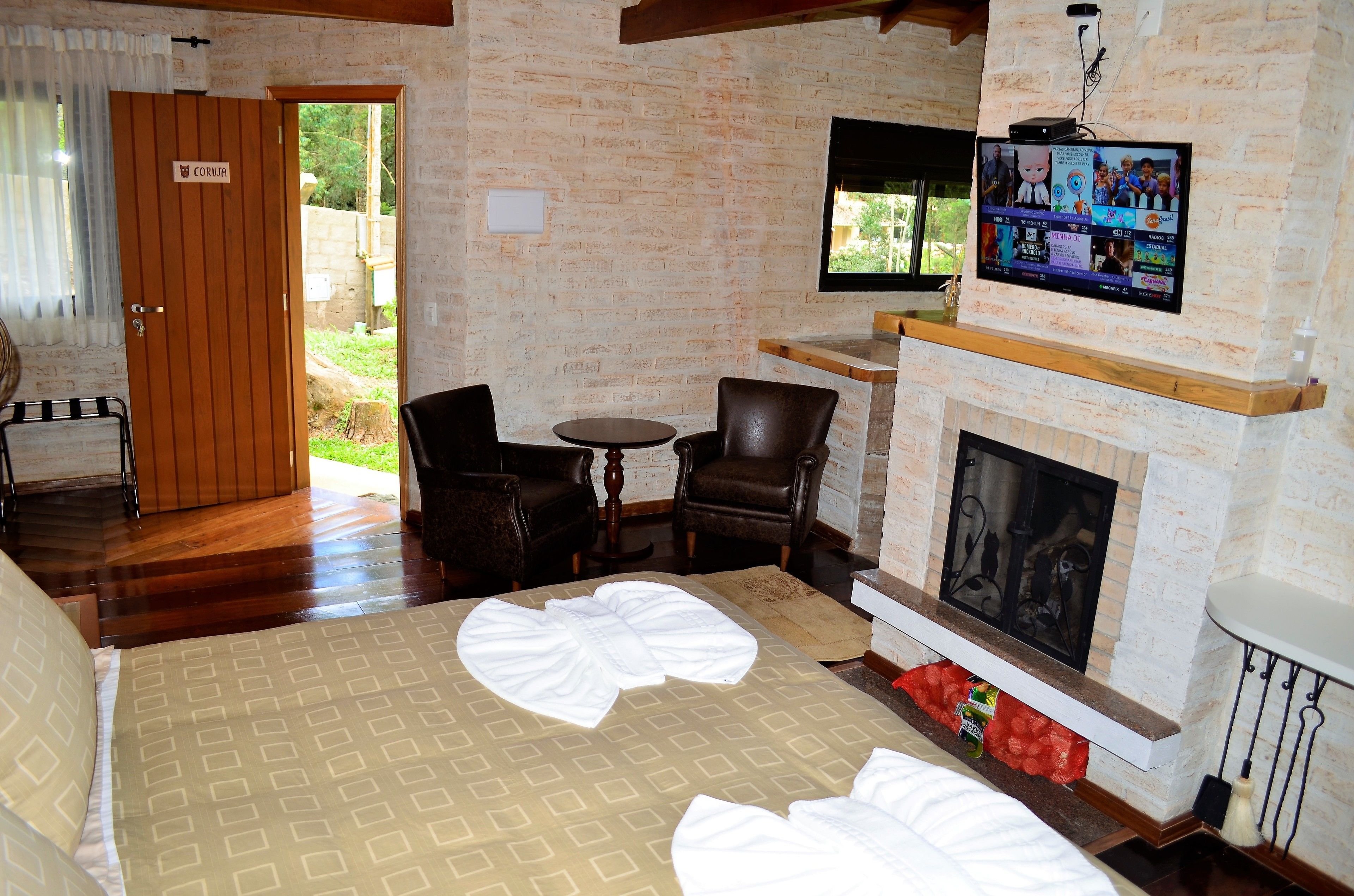 A room with a fireplace, a television mounted above it, and a bed with neatly folded white towels.