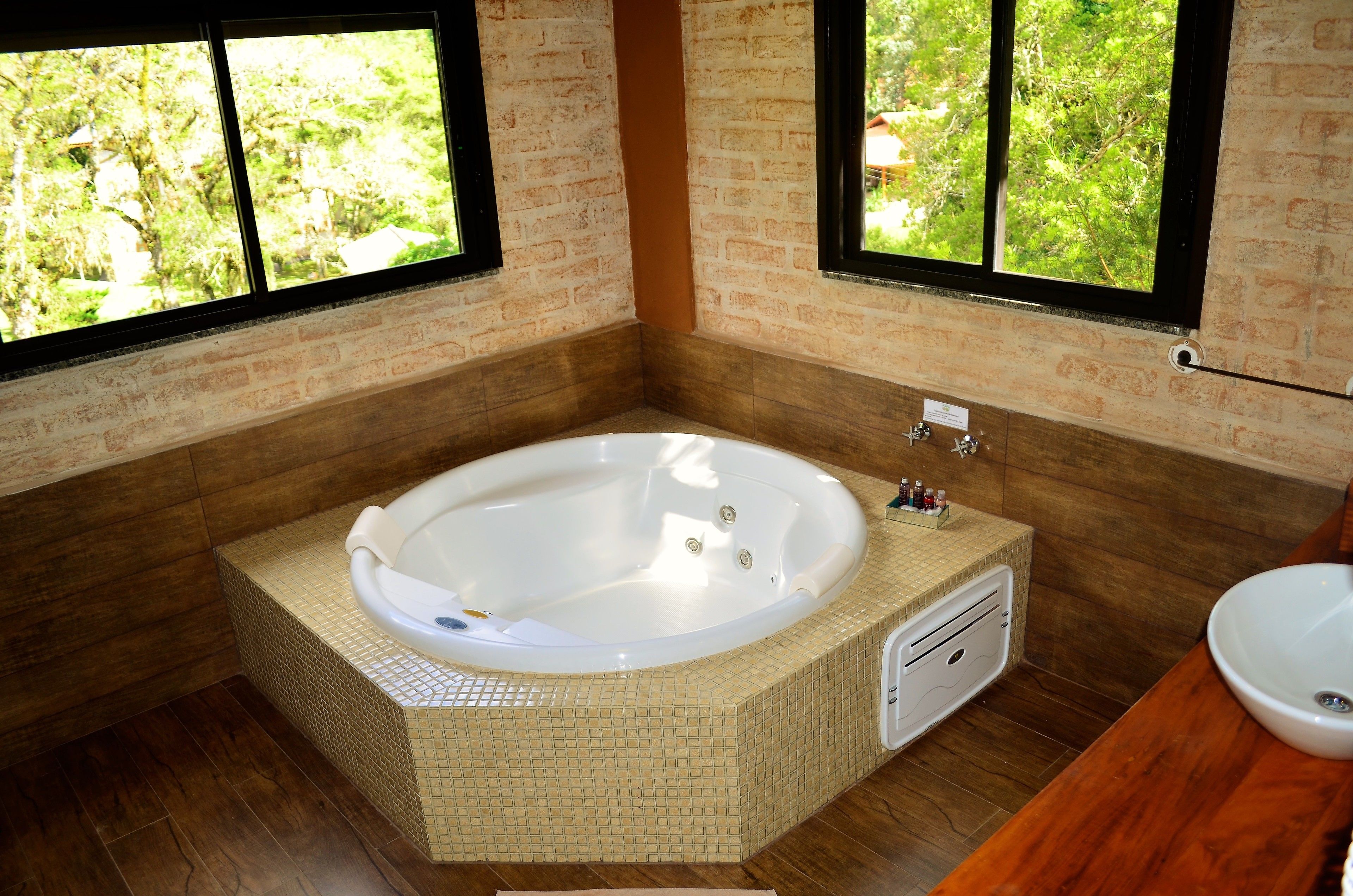 Un baño con una bañera grande, un tocador de madera y un ventanal con vistas al verdor.