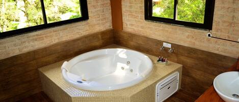 Un baño con una bañera grande, un tocador de madera y un ventanal con vistas al verdor.