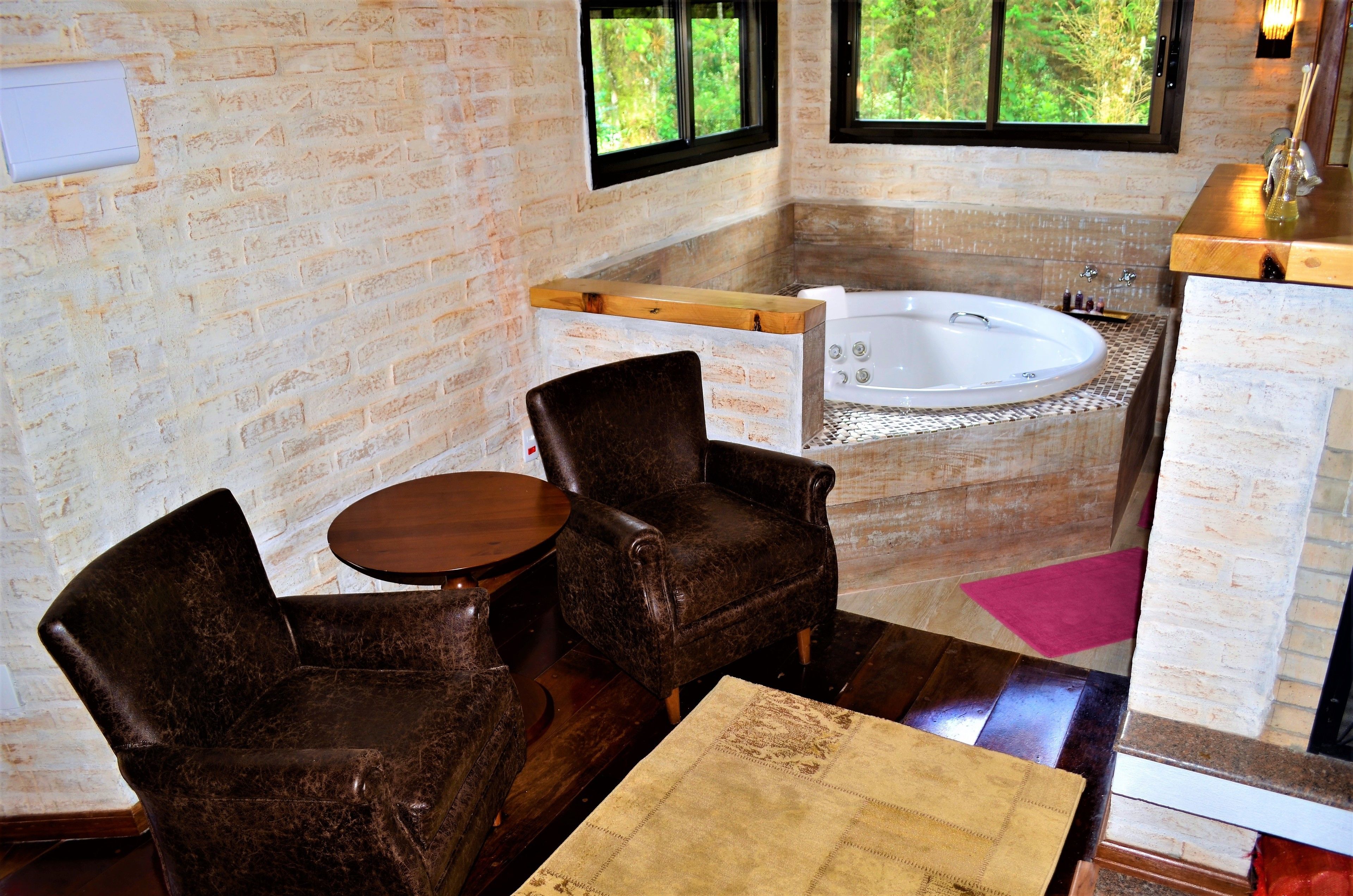 Un baño con bañera, dos sillas, una mesa de madera y una ventana con vistas a árboles.