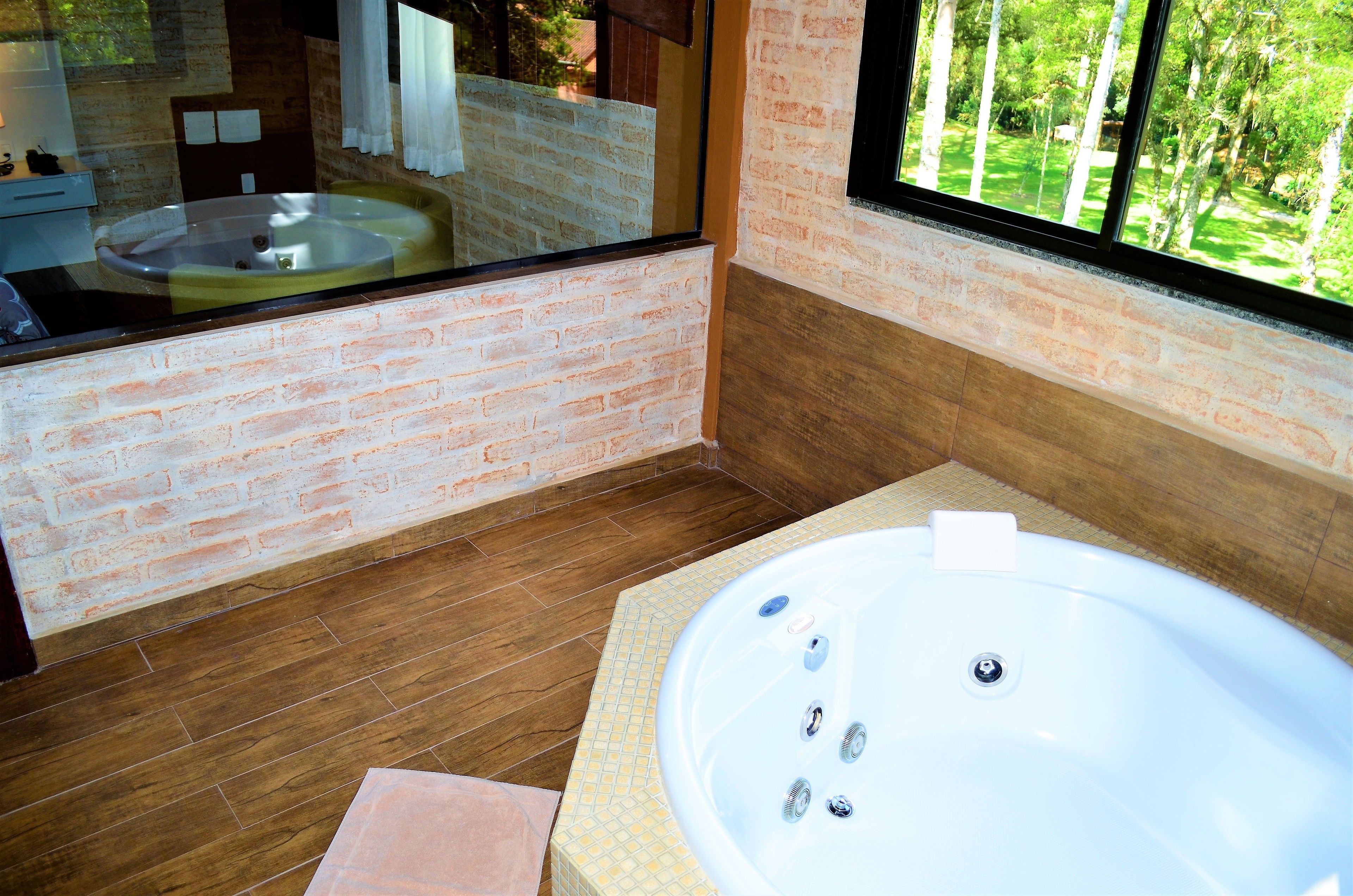 A modern bathroom with a large bathtub, a mirror, and a view of greenery outside.