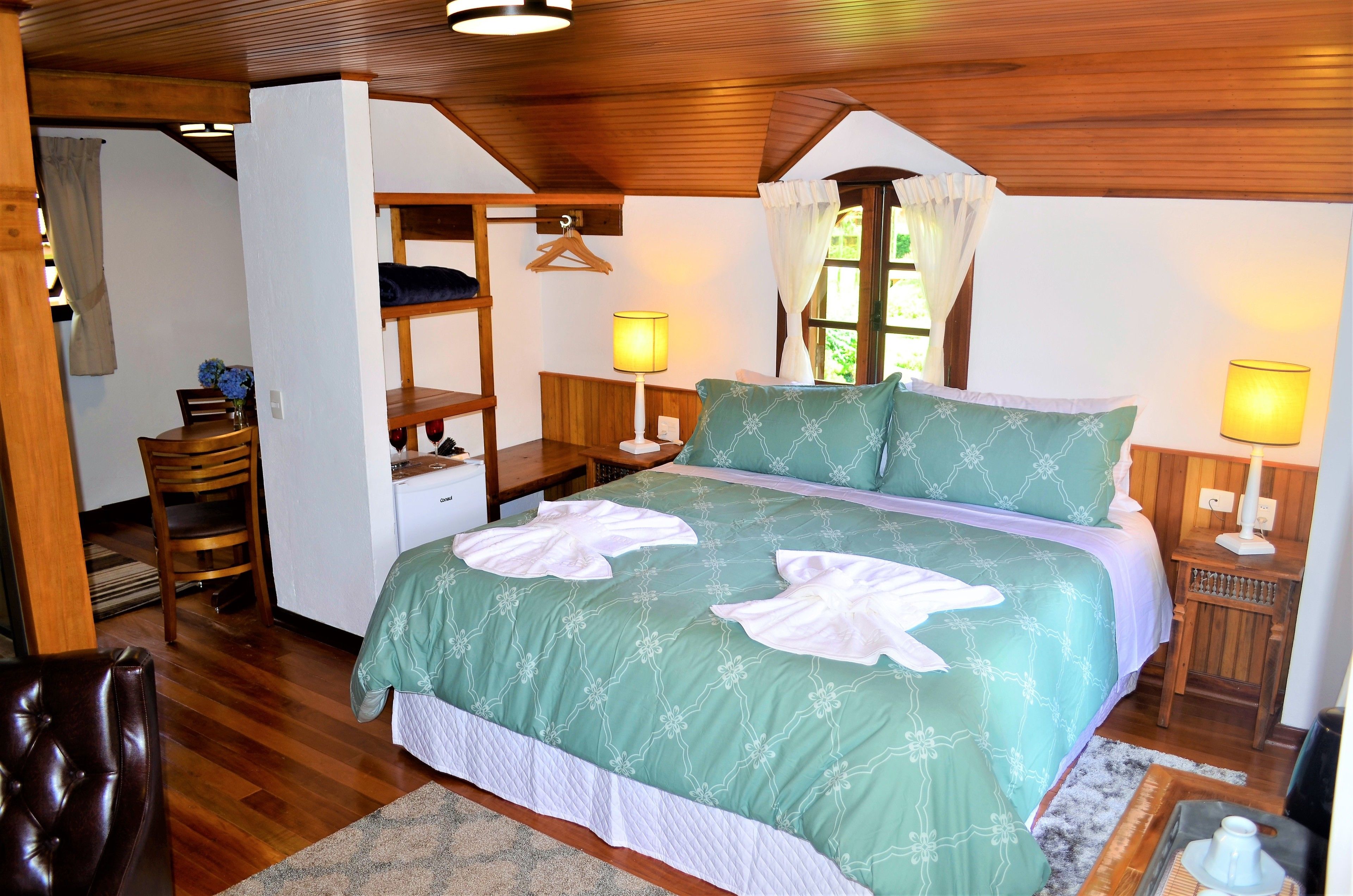 A bedroom with a bed, bedside tables, a chair, a wardrobe, and a window with curtains.