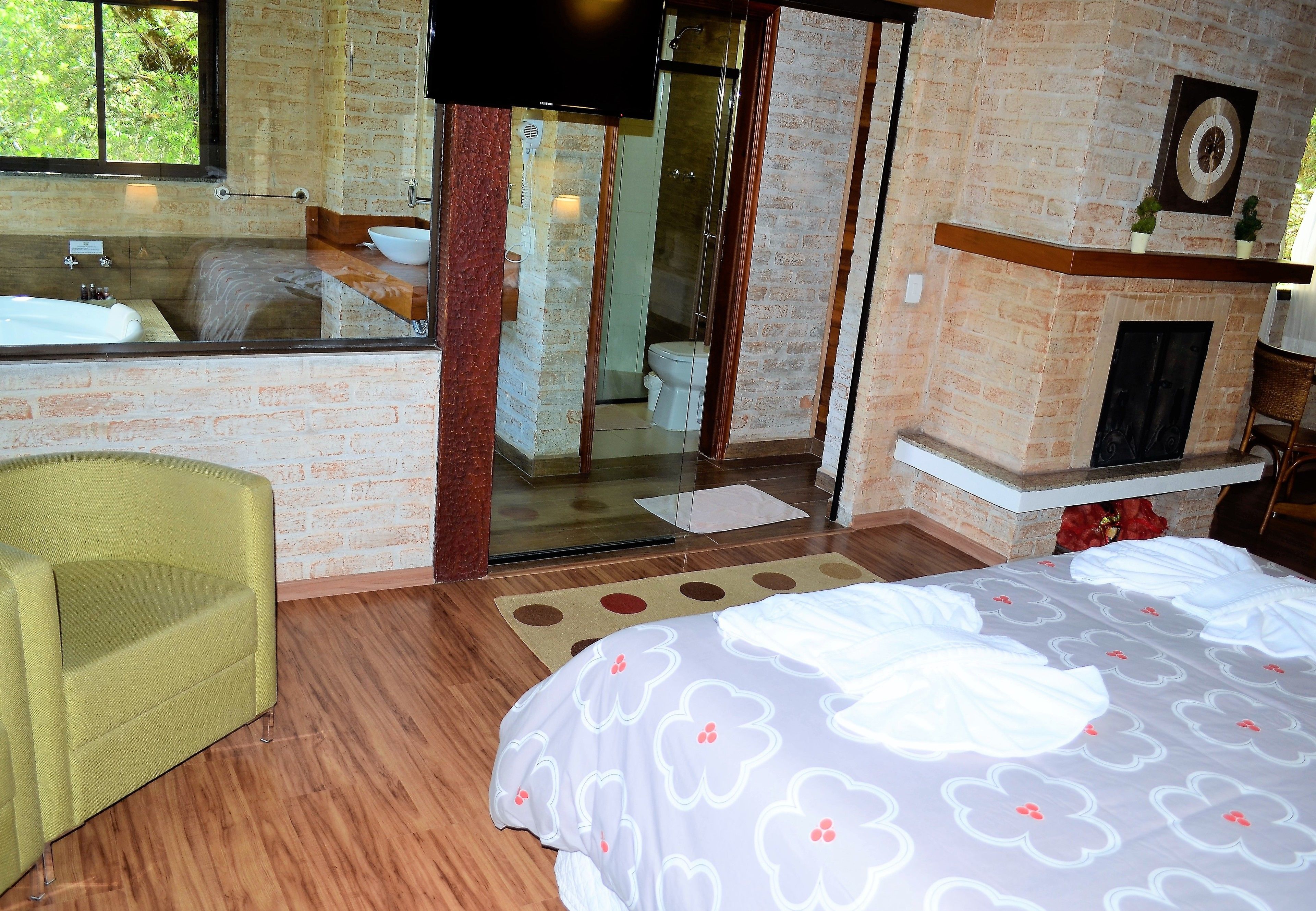 Una habitación de hotel con una cama grande, una zona de estar con una silla, un baño con bañera, ducha y chimenea.