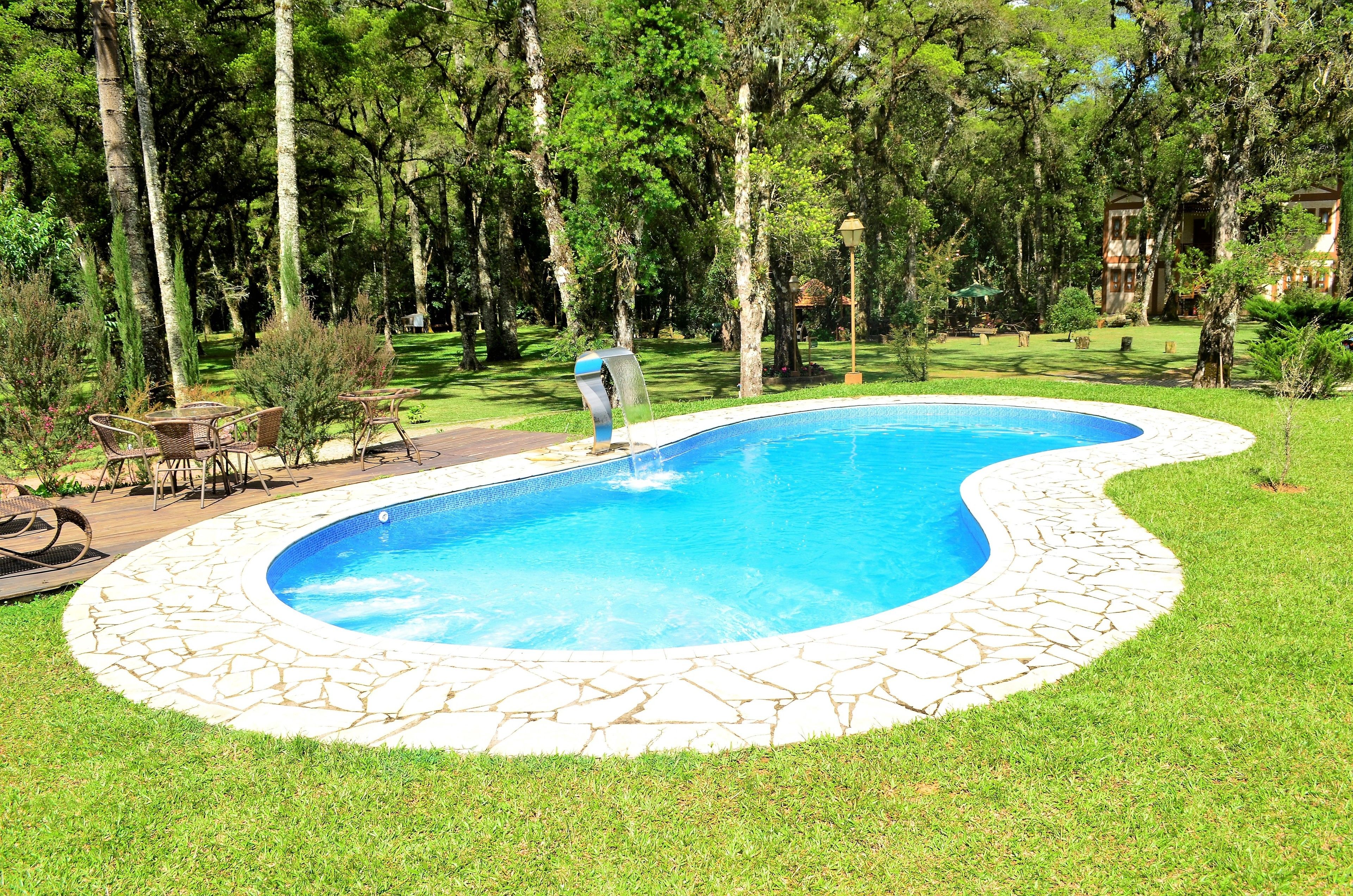 Une piscine bordée de pierres, entourée d’une pelouse et d’arbres.