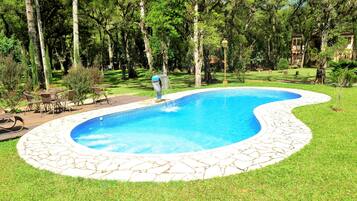 Une piscine bordée de pierres, entourée d’une pelouse et d’arbres.