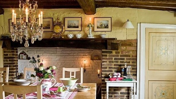 A rustic dining area with a wooden table set for two, a chandelier, and a stone fireplace. - The Old Manor House B & B (Westerham)