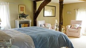 A bedroom with a large bed, a chair, a small table with a pitcher, and a fireplace. - The Old Manor House B & B (Westerham)