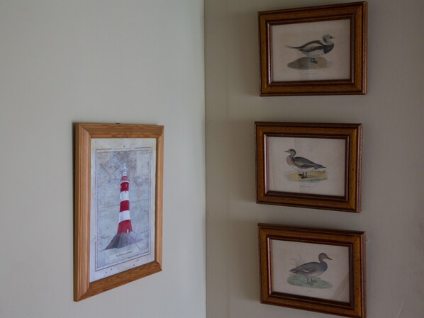 Un mur orné de quatre tableaux encadrés, dont un représentant un phare et trois oiseaux.