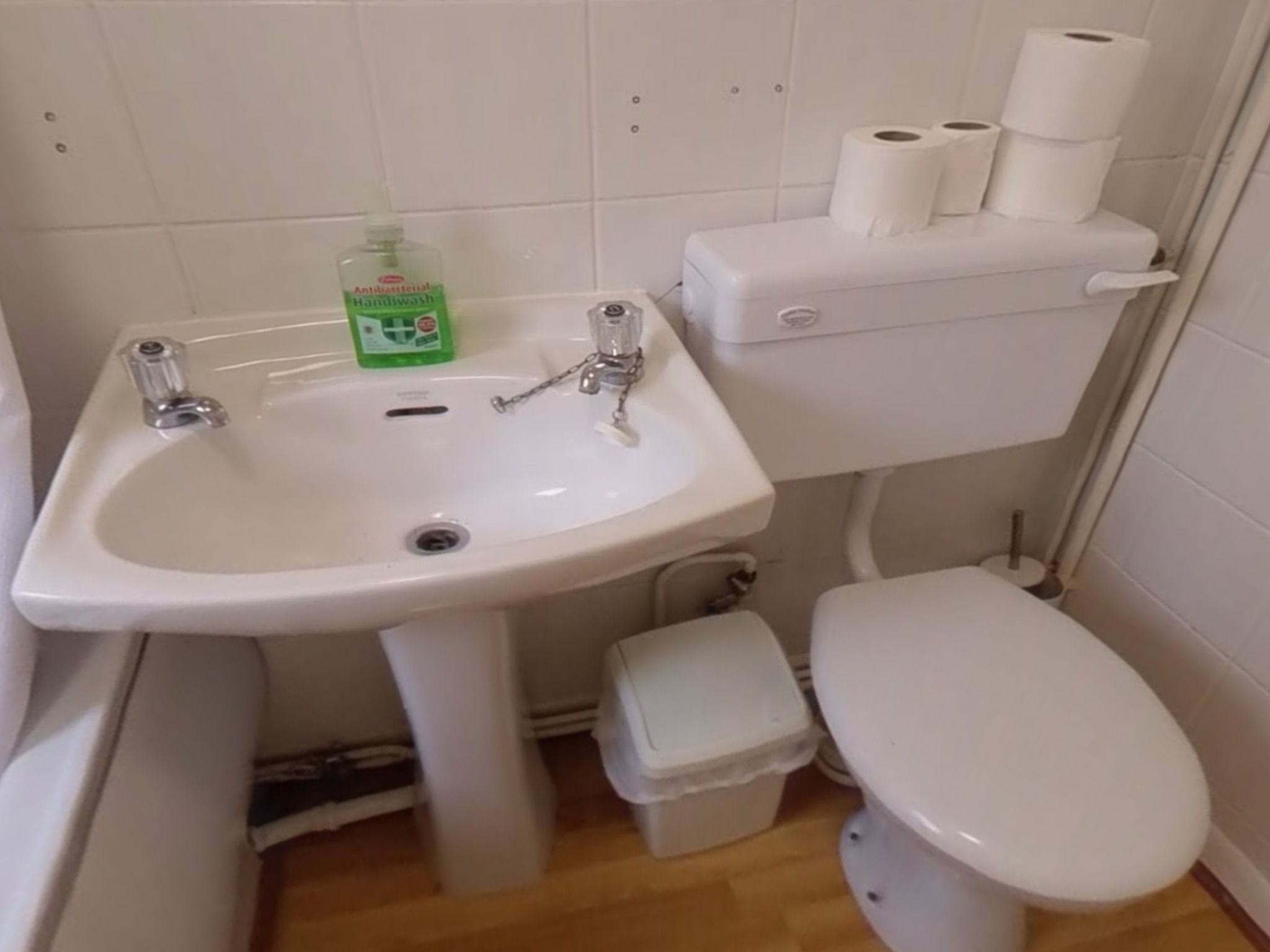 A small bathroom with a white sink, toilet, and a trash bin.