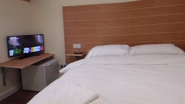 Hotellihuone, jossa on sänky, televisio puisen jalustan päällä ja pieni työpöytä.