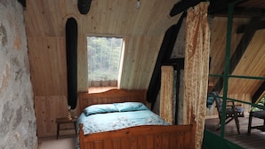 Ein Zimmer aus Holz mit einem Bett, einem Fenster und Blick ins Freie.
