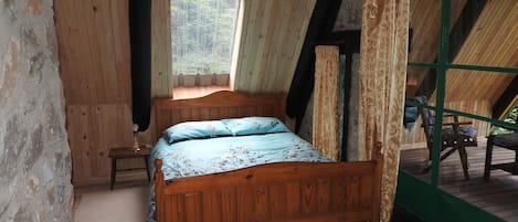 A wooden room with a bed, a window, and a view of the outdoors.
