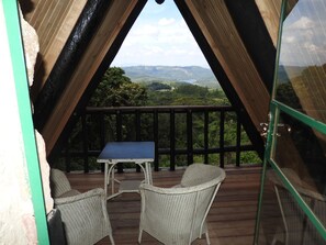 An outdoor deck with a table and two chairs, overlooking a mountainous landscape.