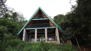 Ein rustikales Chalet mit Stein Fundament, Holzbalken und einem grünen Dach, umgeben von dichtem Grün.