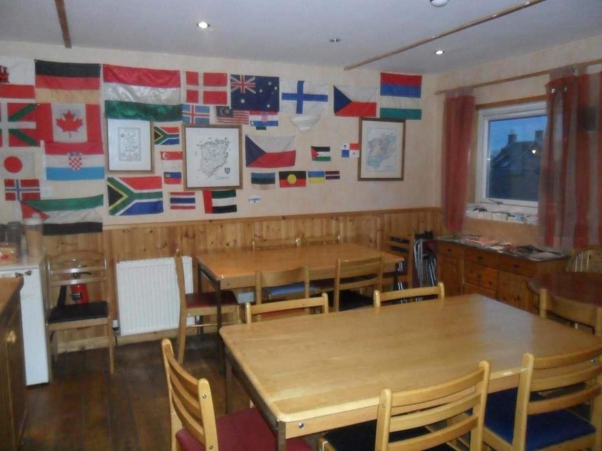 Comedor con mesas y sillas de madera, área de cocina con radiador, y paredes decoradas con varias banderas nacionales.