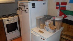 Una cocina con estufa, horno y refrigerador. Hay alimentos y recipientes sobre el refrigerador.