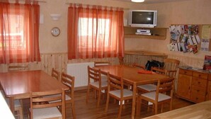 Un comedor con mesas y sillas de madera, un televisor en una estantería y un tablón de anuncios con papeles.