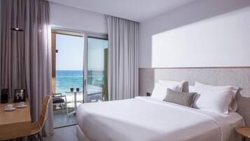Ein Hotelzimmer mit einem großen Bett, einem Schreibtisch mit Kaffeemaschine und Meerblick durch eine Glastür.