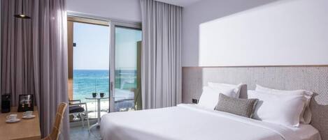 A hotel room with a large bed, a desk with a coffee maker, and a view of the ocean through a sliding glass door.