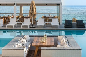 Un área junto a la piscina con sillones de descanso, una mesa de madera y vista al mar.
