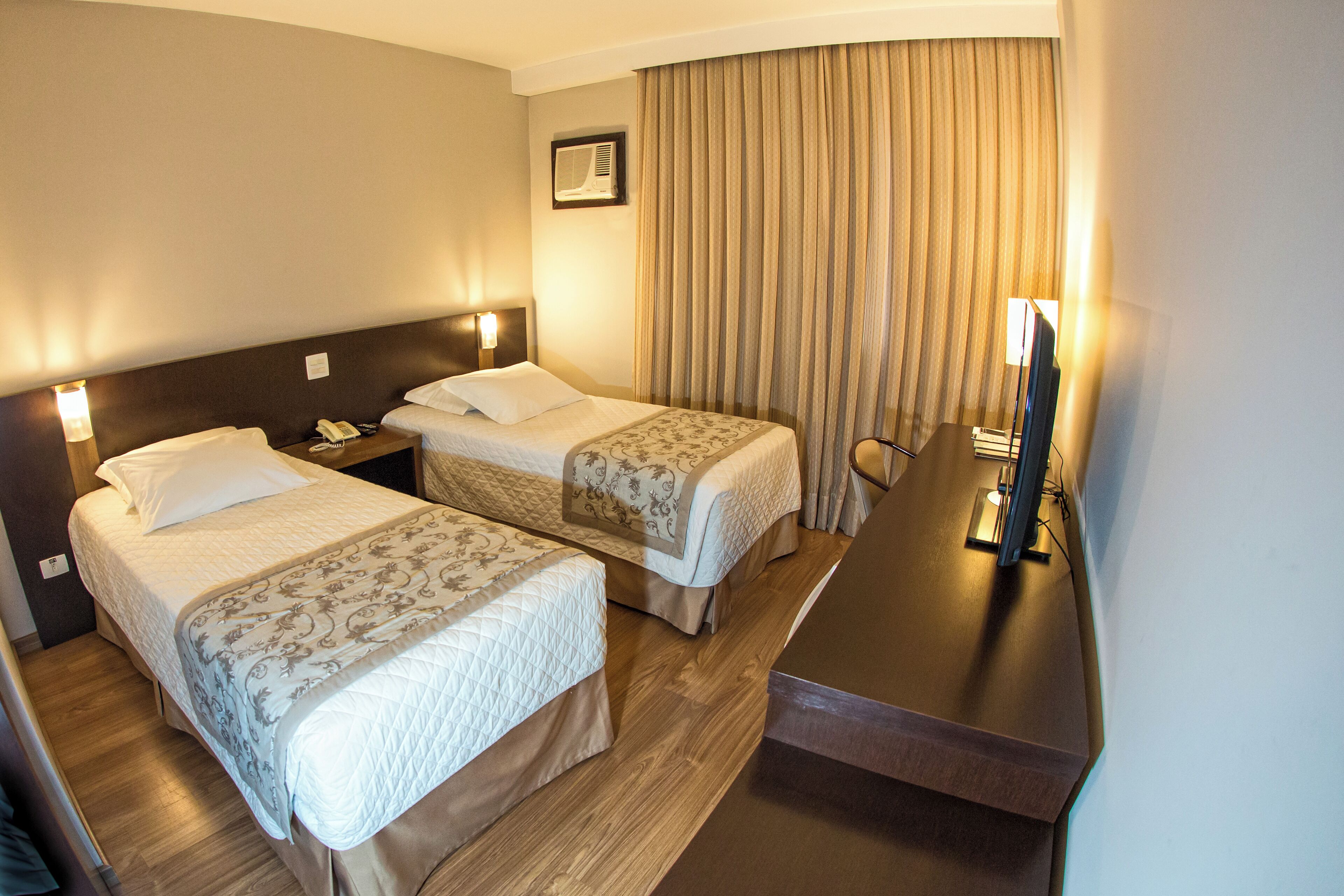A hotel room with two beds, a desk, a chair, a television, and a curtain.
