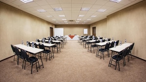 Un salón de conferencias con varias mesas y sillas, equipado con botellas de agua, dispuesto en una distribución simétrica.