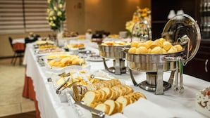 Una mesa de bufé con diversos alimentos, incluyendo pan, pasteles y un recipiente grande que parece contener natillas o pudín.