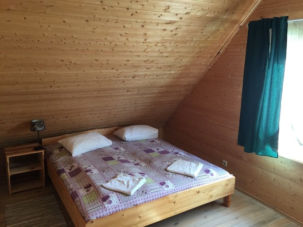 Un lit simple dans une pièce en bois avec un plafond en pente, une table de chevet et une fenêtre avec des rideaux.